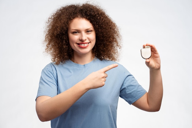 Foto una mujer atractiva y sonriente con el cabello rizado sosteniendo un marcapasos señalando con el dedo mirando a la cámara