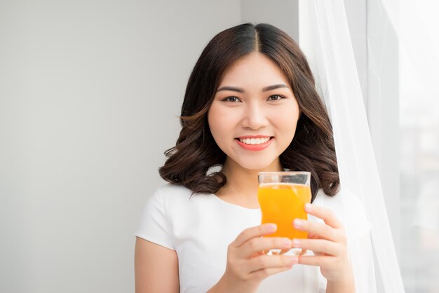 Mujer atractiva sosteniendo un vaso de jugo de naranja mientras está de pie en la cocina