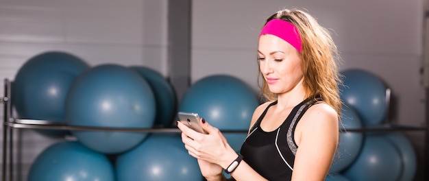 Mujer atractiva con teléfono celular y rastreador de fitness en el gimnasio.