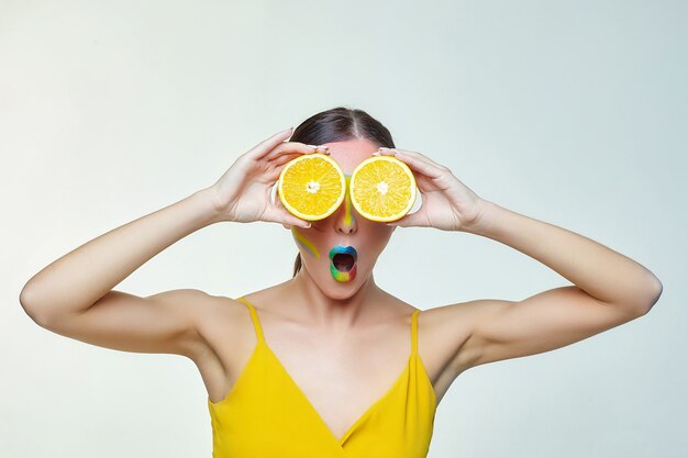 Mujer atractiva tiene rodajas de naranja frente a su cara