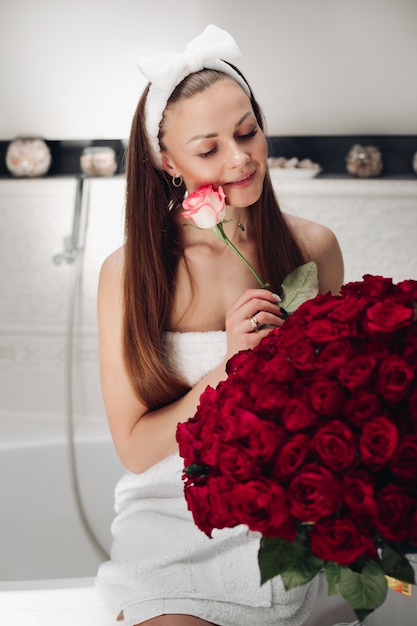 Mujer atractiva en toalla y diadema con ramo de rosas rojas.