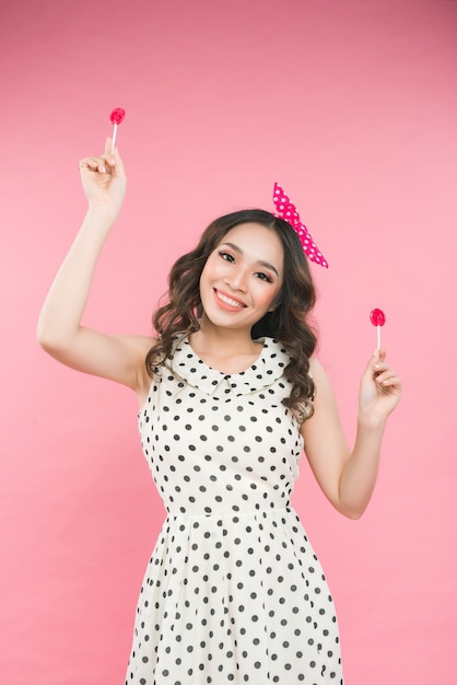 Mujer atractiva en top blanco con piruleta en mano sobre fondo rosa