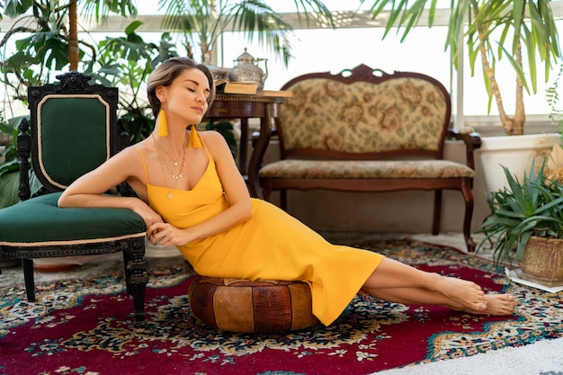 Mujer atractiva en vestido amarillo de verano con peinado corto en la habitación interior de estilo vintage boho posando