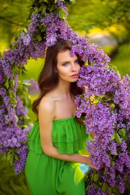 mujer atractiva en vestido verde posando junto a la decoración de flores de color lila.