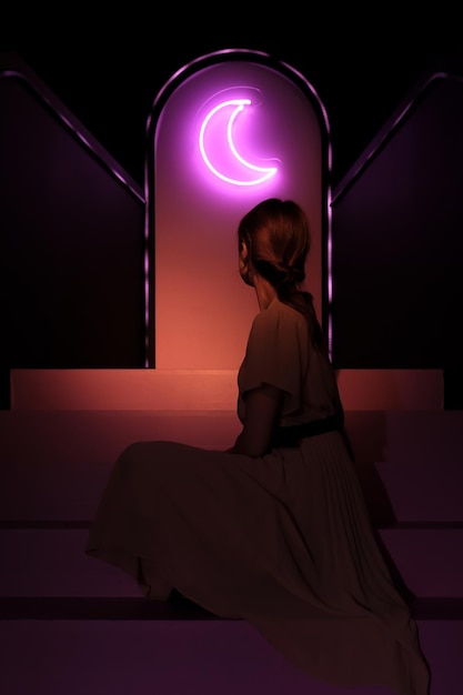 Mujer de atrás con una luz de neón en forma de luna