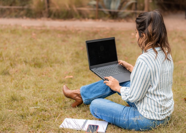 Mujer de atrás sentada en el césped trabajando en su computadora portátil