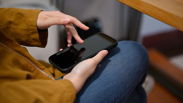 La mujer con atuendo causal se relaja sentada en la cafetería y usa su teléfono inteligente moderno