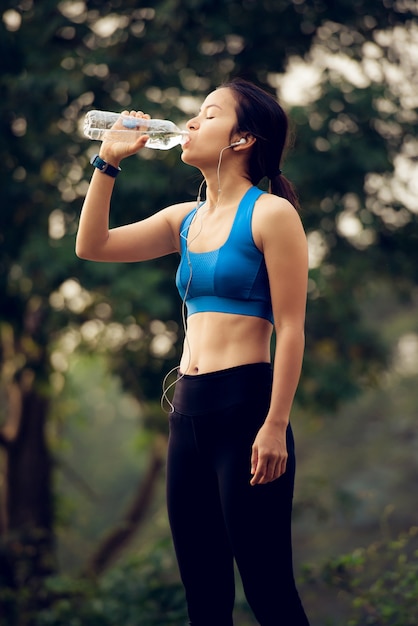 Mujer con auriculares agua potable después del ejercicio