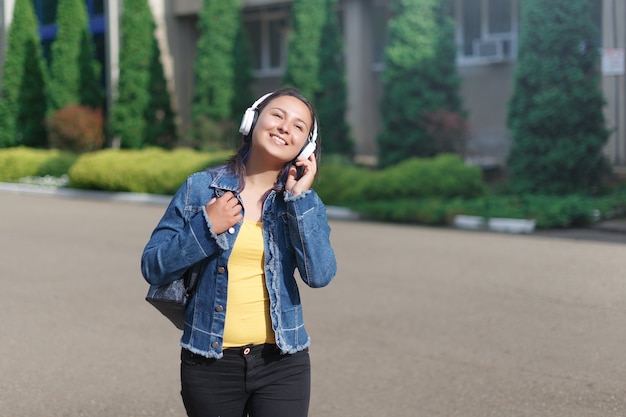 Mujer con auriculares caminando en el parque en un día soleado y escuchando música