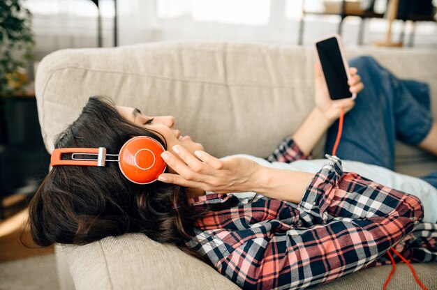 Mujer en auriculares escuchando música en el sofá.