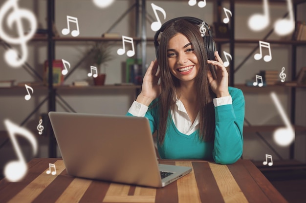 Una mujer con auriculares está sentada en la mesa de madera con una laptop gris