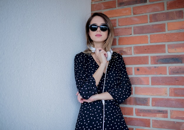 Mujer con auriculares y gafas de sol en la pared de ladrillo