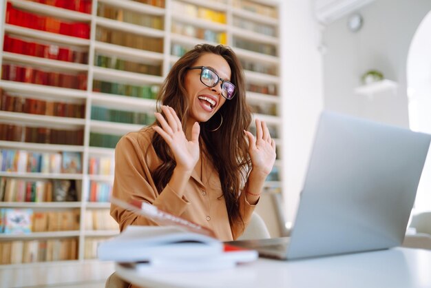 Mujer con auriculares inalámbricos llamando en una computadora portátil hablando por cámara web sentada en un café moderno Educación