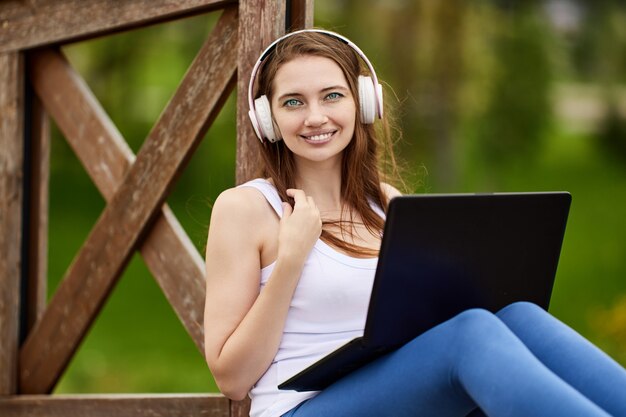 Mujer en auriculares inalámbricos tiene teletrabajo con portátil al aire libre