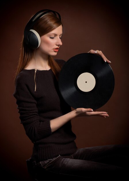 Mujer con auriculares mirando el viejo disco de gramófono en sus manos sobre fondo marrón oscuro