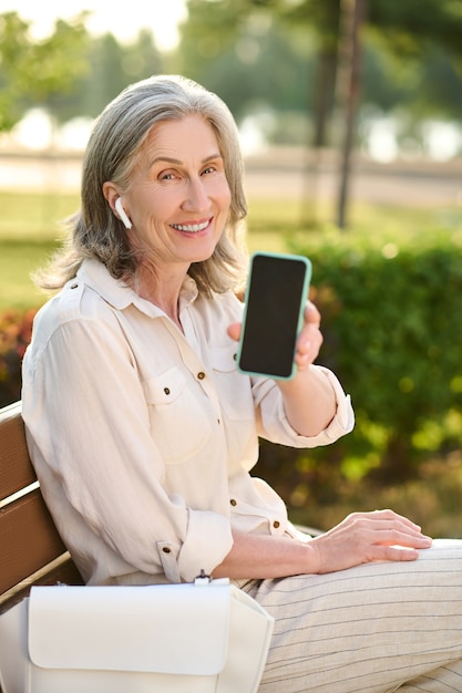 Mujer en auriculares mostrando la pantalla del teléfono inteligente