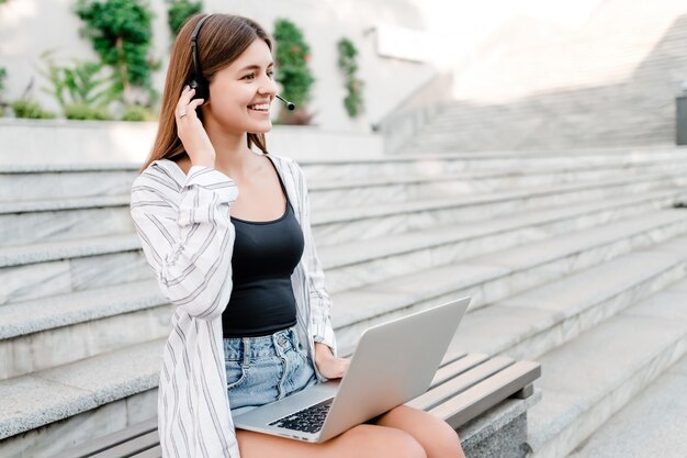 Mujer con auriculares y portátil en el banco al aire libre