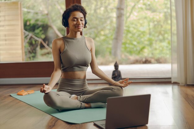 Mujer con auriculares practicando yoga y escuchando meditación en casa sentada en la postura del loto en la alfombra