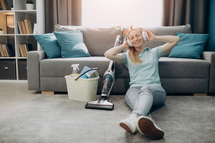 Mujer con auriculares tomando un descanso durante la limpieza de una habitación acogedora