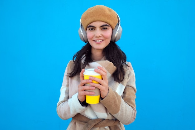 Mujer con auriculares y vaso de papel mirando a la cámara