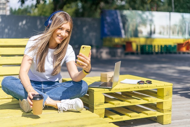 Mujer en auriculares con una videollamada. Niña feliz y sonriente trabajando afuera y tomando café