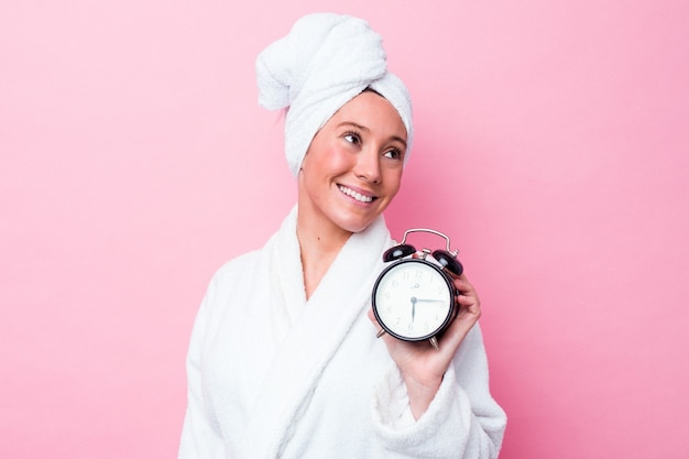 La mujer australiana joven que sale tarde de la ducha aislada en fondo rosado mira a un lado sonriente, alegre y agradable.