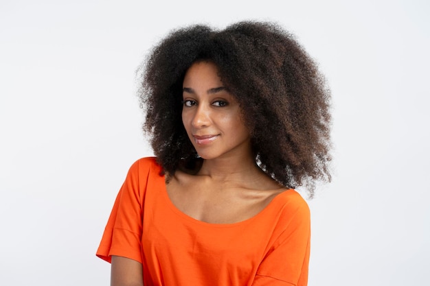 Mujer auténtica y amigable con el pelo rizado vistiendo una camiseta naranja con el pelo rizado mirando a la cámara Concepto de procedimientos de champú cosmético para el cuidado del cabello