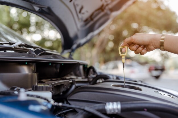 Una mujer de autoservicio utiliza la varilla medidora para comprobar el nivel de aceite del motor del vehículo del automóvil mantenimiento profesional