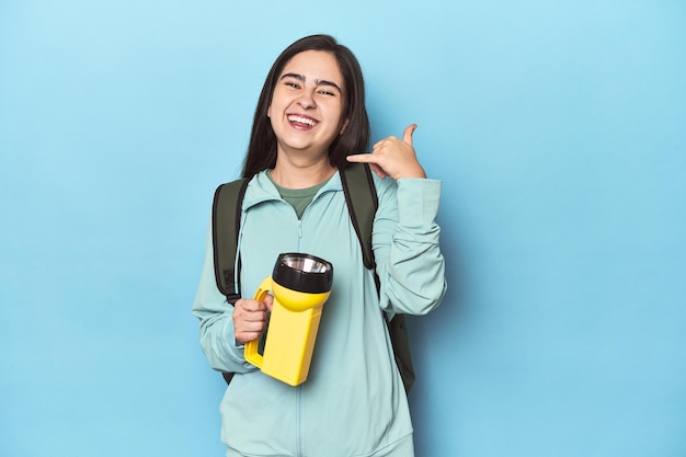 Foto mujer aventurera con mochila en azul mostrando un gesto de llamada de teléfono móvil con los dedos