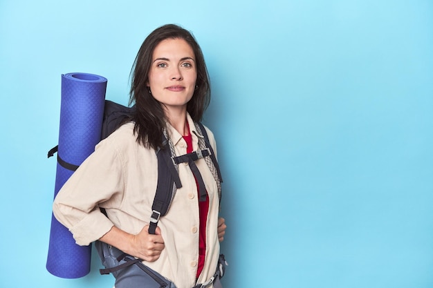 Foto mujer aventurera con mochila y colchoneta en azul.