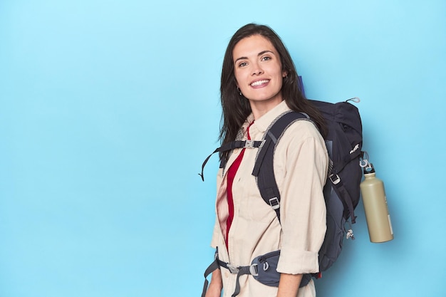 Mujer aventurera con mochila y colchoneta en azul.