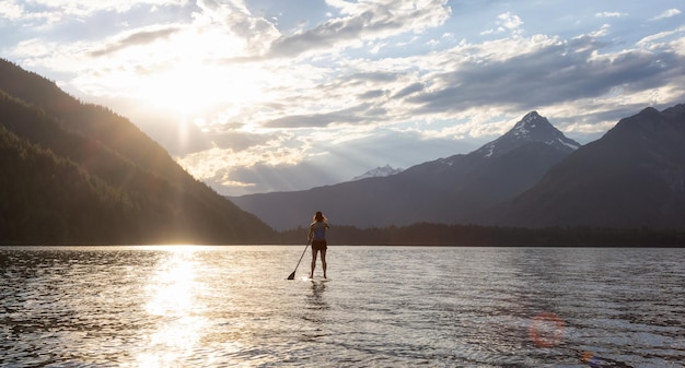 Mujer aventurera remando en un lago alrededor del paisaje montañoso canadiense