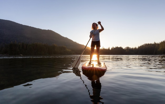 Mujer aventurera remando en una tabla de paddle en un lago tranquilo