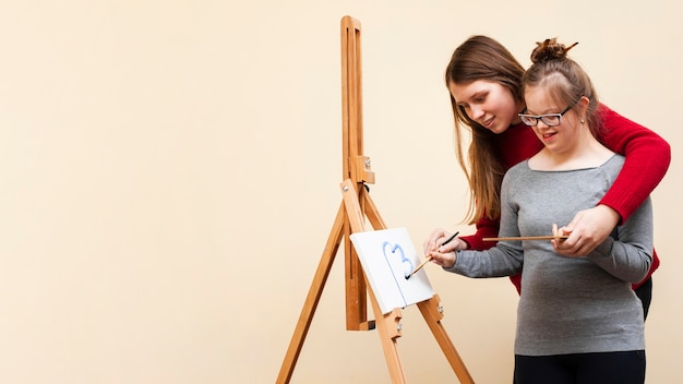 Foto mujer ayudando a niña sonriente con pintura de síndrome de down