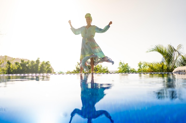 Mujer bailando con vestido largo junto a una piscina