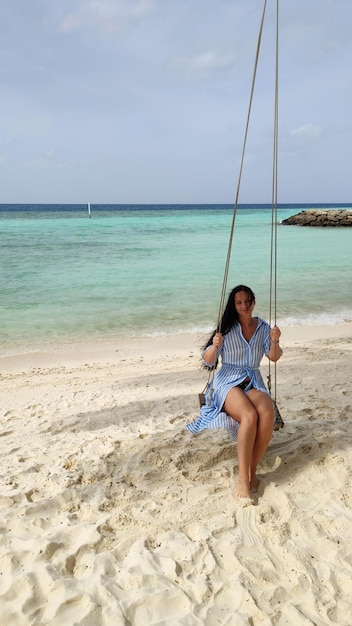 Una mujer se balancea en un columpio colgado de una palmera Mar turquesa y playa de arena blancaxA