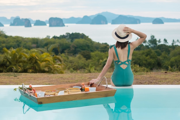 Mujer con bandeja de desayuno flotante en el hotel con piscina de lujo