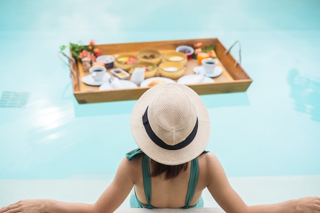 Mujer con bandeja de desayuno flotante en el hotel con piscina de lujo