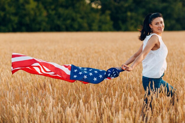 Mujer con bandera americana en campo de trigo al atardecer