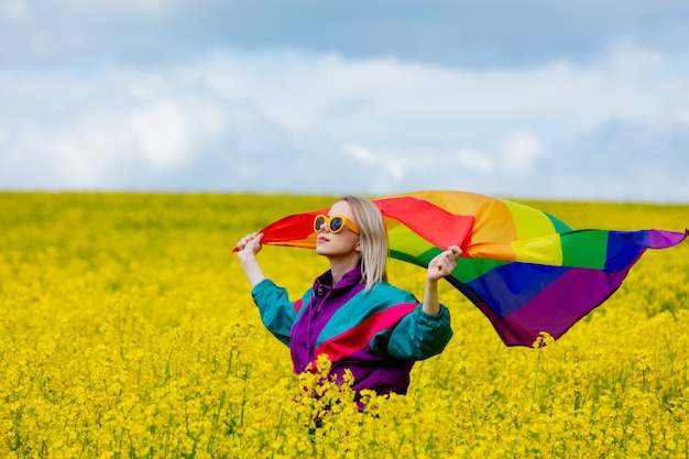 Mujer con bandera arco iris LGBT en campo de colza amarillo en primavera