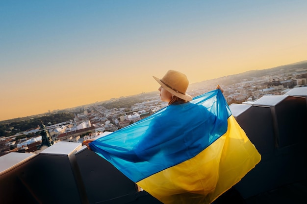 Una mujer se para con la bandera nacional ucraniana y la ondea rezando por la paz al atardecer en LvivxAA símbolo de la independencia y la fuerza del pueblo ucraniano Oren por Ucrania