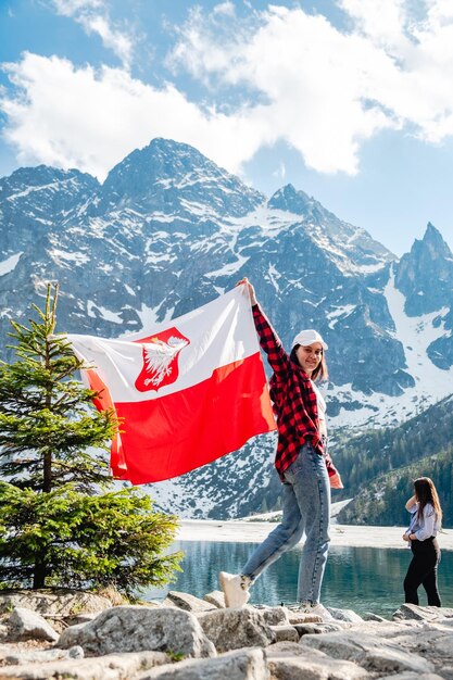 Una mujer con la bandera de Polonia está parada en la orilla de un lago Morskie Oko