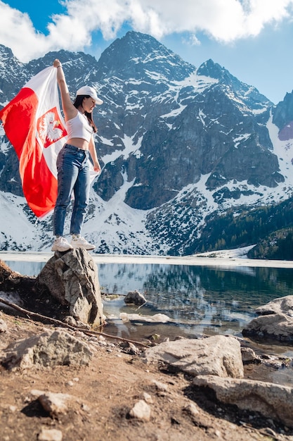 Una mujer con la bandera de Polonia está parada en la orilla de un lago Morskie Oko