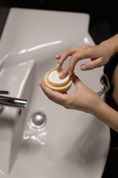 La mujer del baño saca la crema del frasco con los dedos. Concepto de cuidado de la piel.