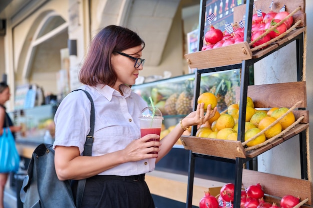 Mujer en el bar de jugos de frutas al aire libre con jugo fresco