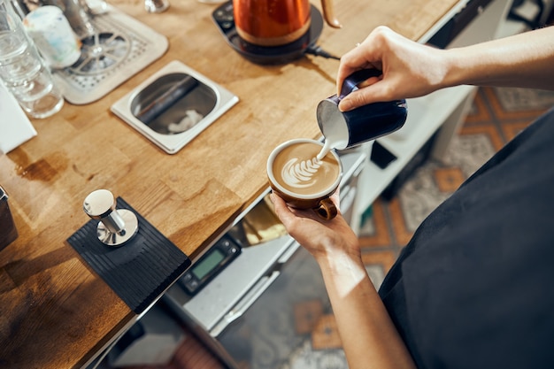 Mujer barista haciendo capuchino, mujer preparando café. Taza de café con arte latte.