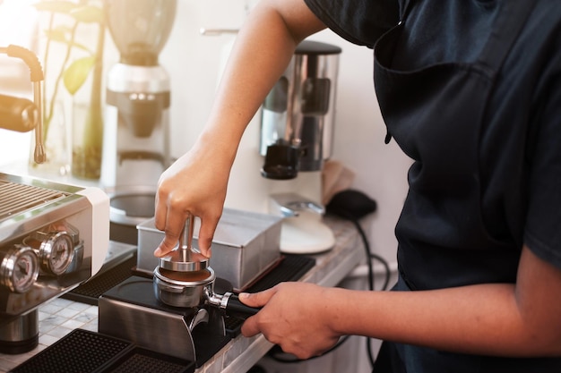 mujer barista lleva delantal y prepara café con máquina para clientes en la cafetería