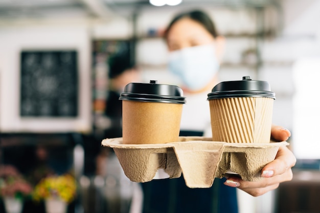 Mujer Barista con una mascarilla que sirve café en vasos desechables de papel para llevar en la cafetería.