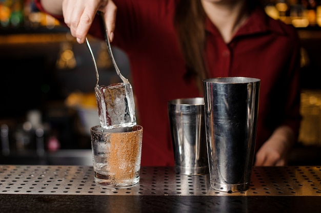 Mujer barman mano poniendo un gran cubo de hielo en una copa de cóctel