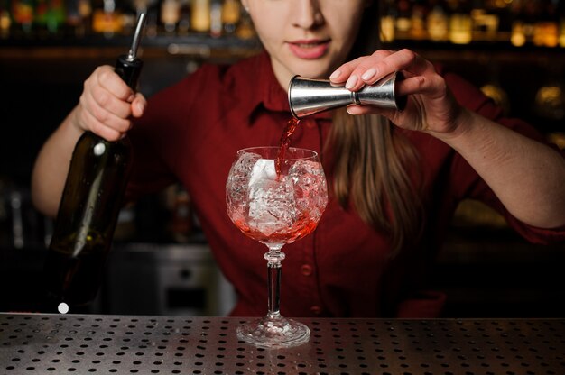 Mujer barman vertiendo amargo en un vaso para hacer un cóctel de jeringas Aperol